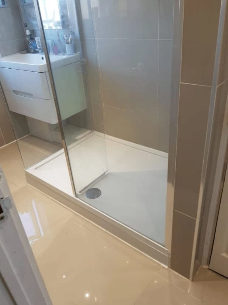 Modern bathroom shower enclosure with glass doors and white tile base, adjacent to a wall-mounted sink in a contemporary bathroom setting