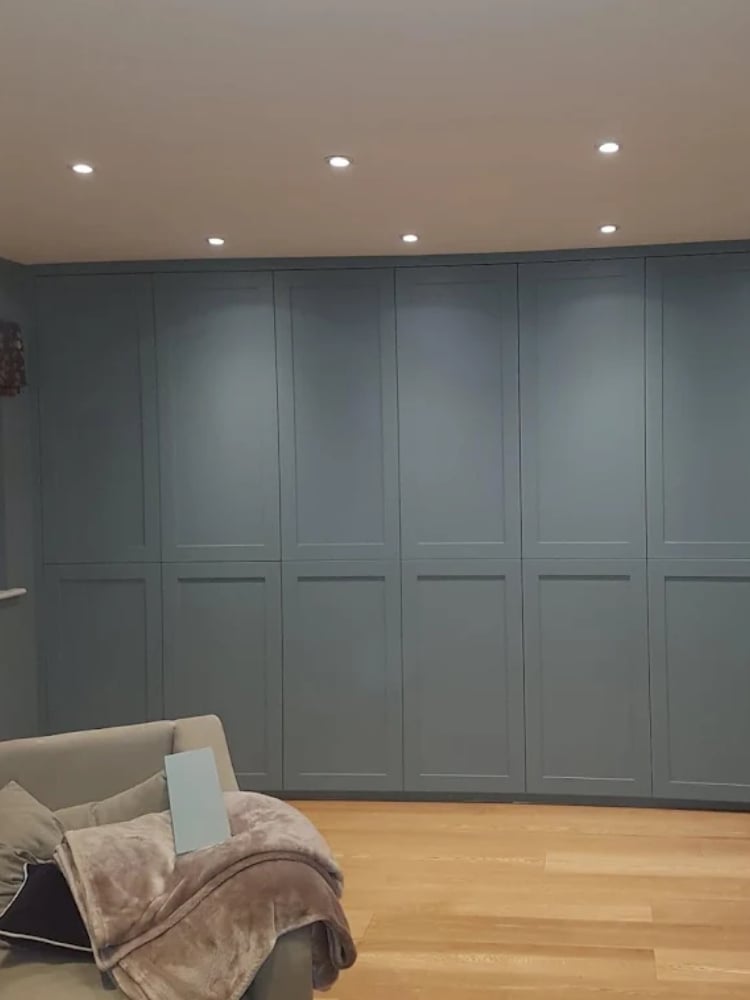 Modern bedroom with gray paneled wardrobe, wooden floor, and cream upholstered chair with throws