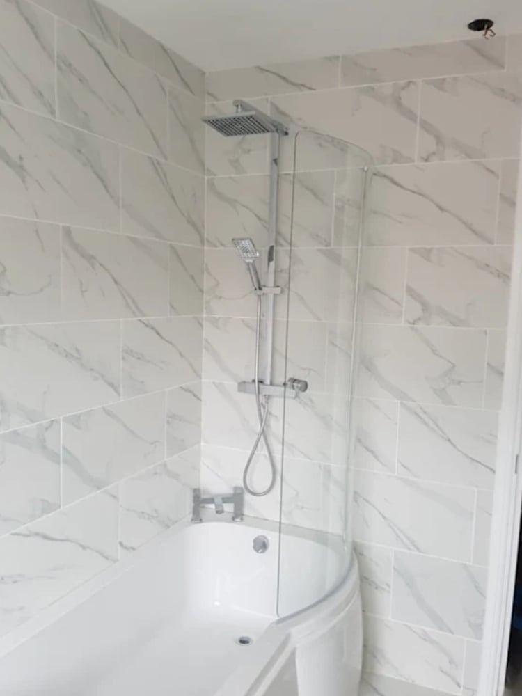 Modern bathroom shower enclosure with white marble tile walls, glass shower door, chrome fixtures, and rainfall showerhead