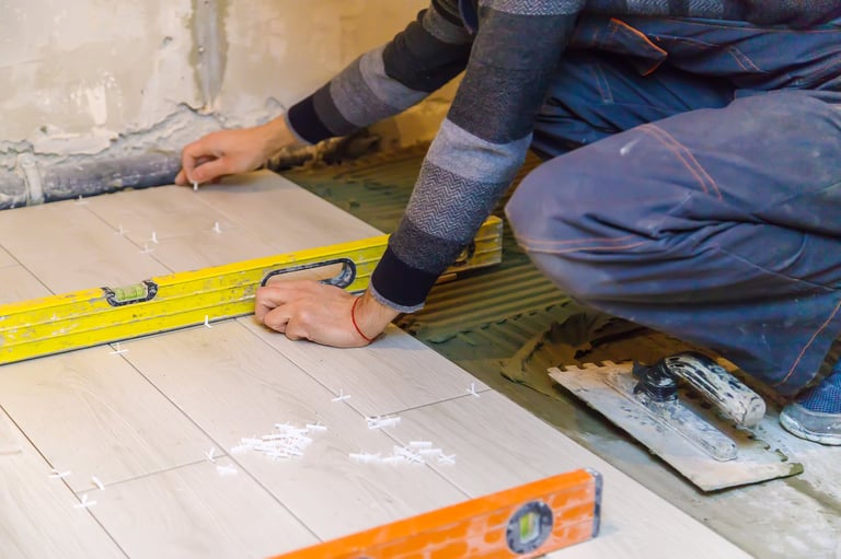 Person using a yellow level tool to measure white tiles on a concrete floor during installation or renovation work
