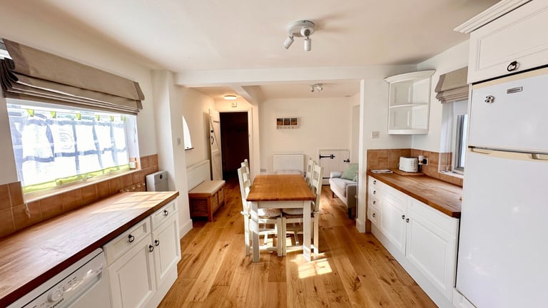 Bright kitchen with white cabinetry, wooden countertops, hardwood flooring, and dining table near window