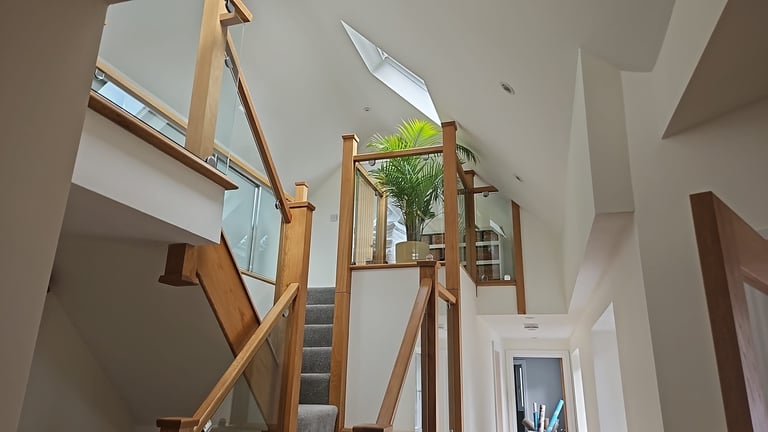 Modern staircase with wooden railings and metal mesh in bright white interior with skylights and potted plant
