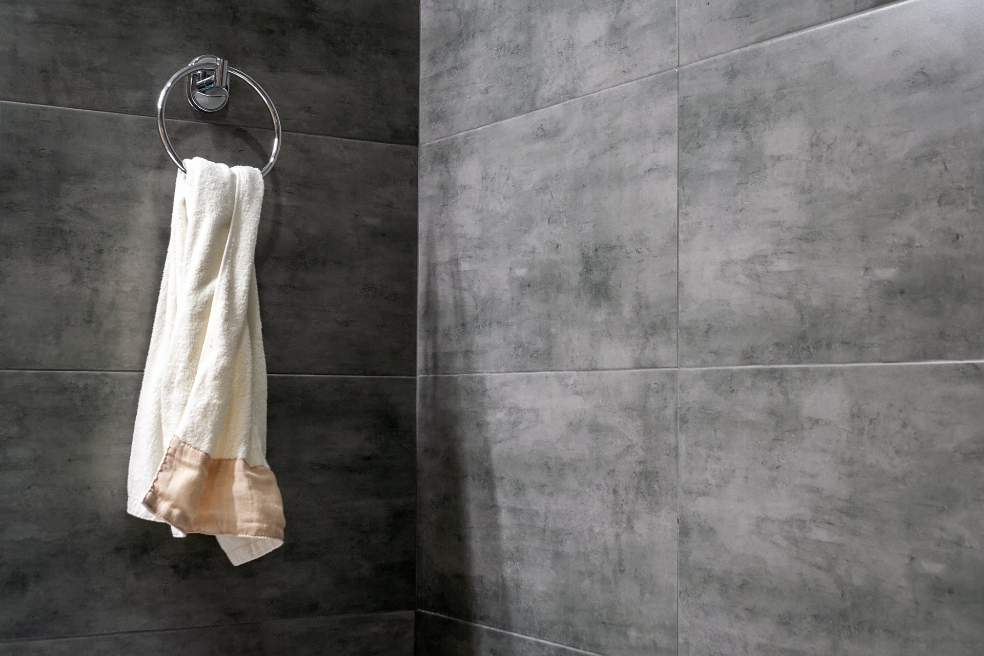 White and peach towel hanging on a chrome ring mounted on a dark gray tile bathroom wall