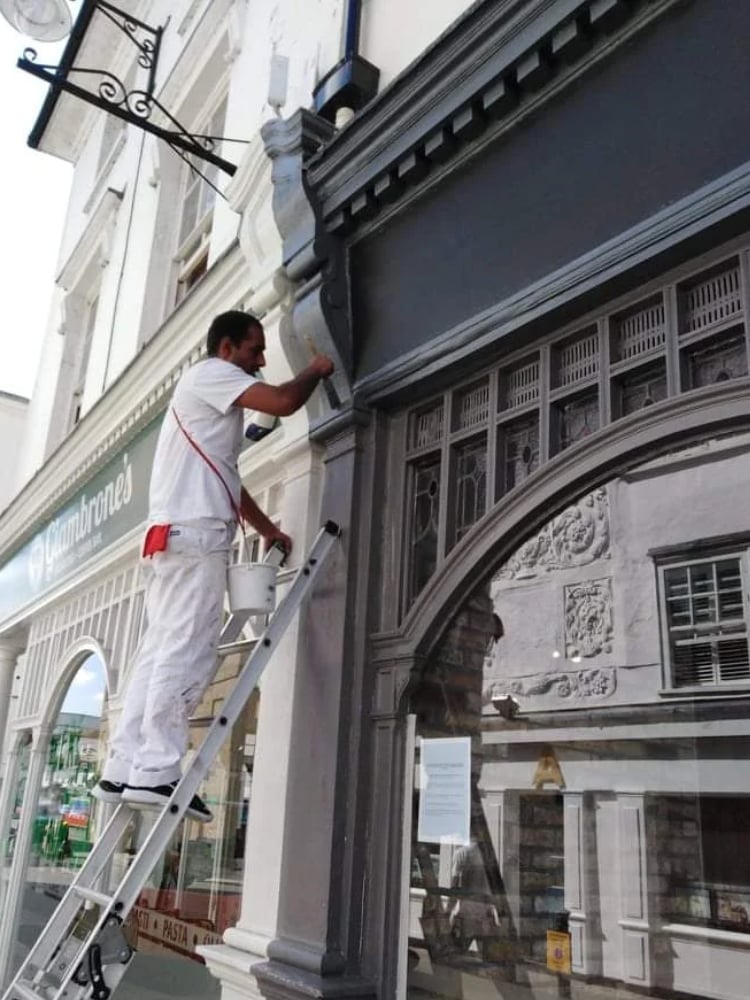 Worker on ladder painting the exterior facade of a historic building storefront